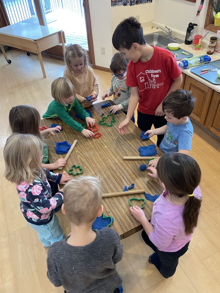 Young children shaping play dough around a classroom table